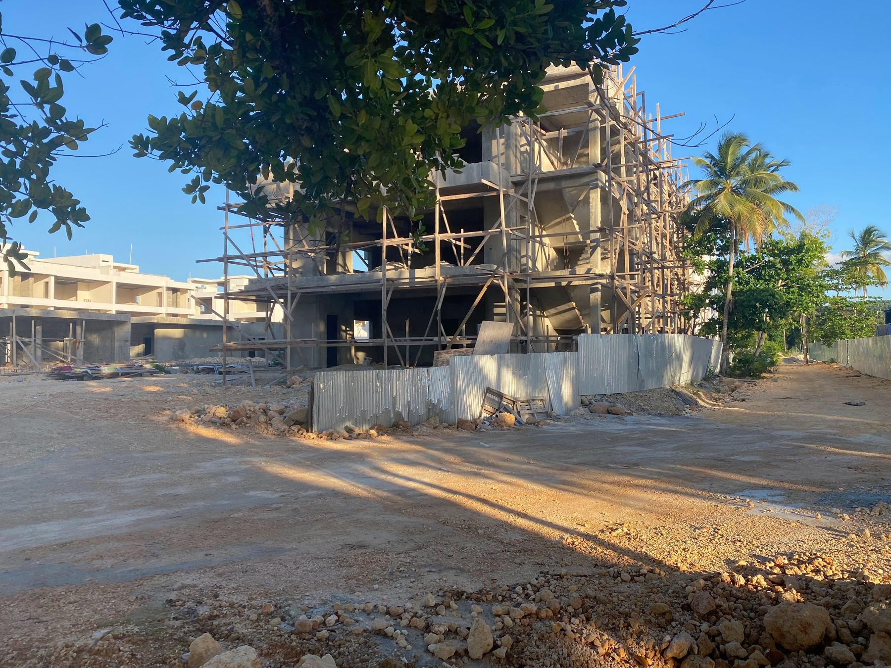 Edificio de varios niveles en construcción, con andamios, detrás de una verja de obra